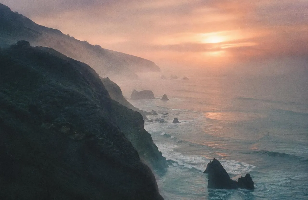 Misty coastal cliffs above the sea at sunrise, washed in soft orange light